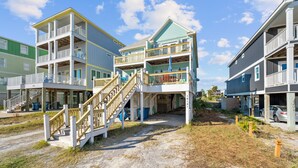 A multi-story beachfront building with balconies, a staircase, and a sandy ground area. - Sea Watch Unit A (Gulf Shores)