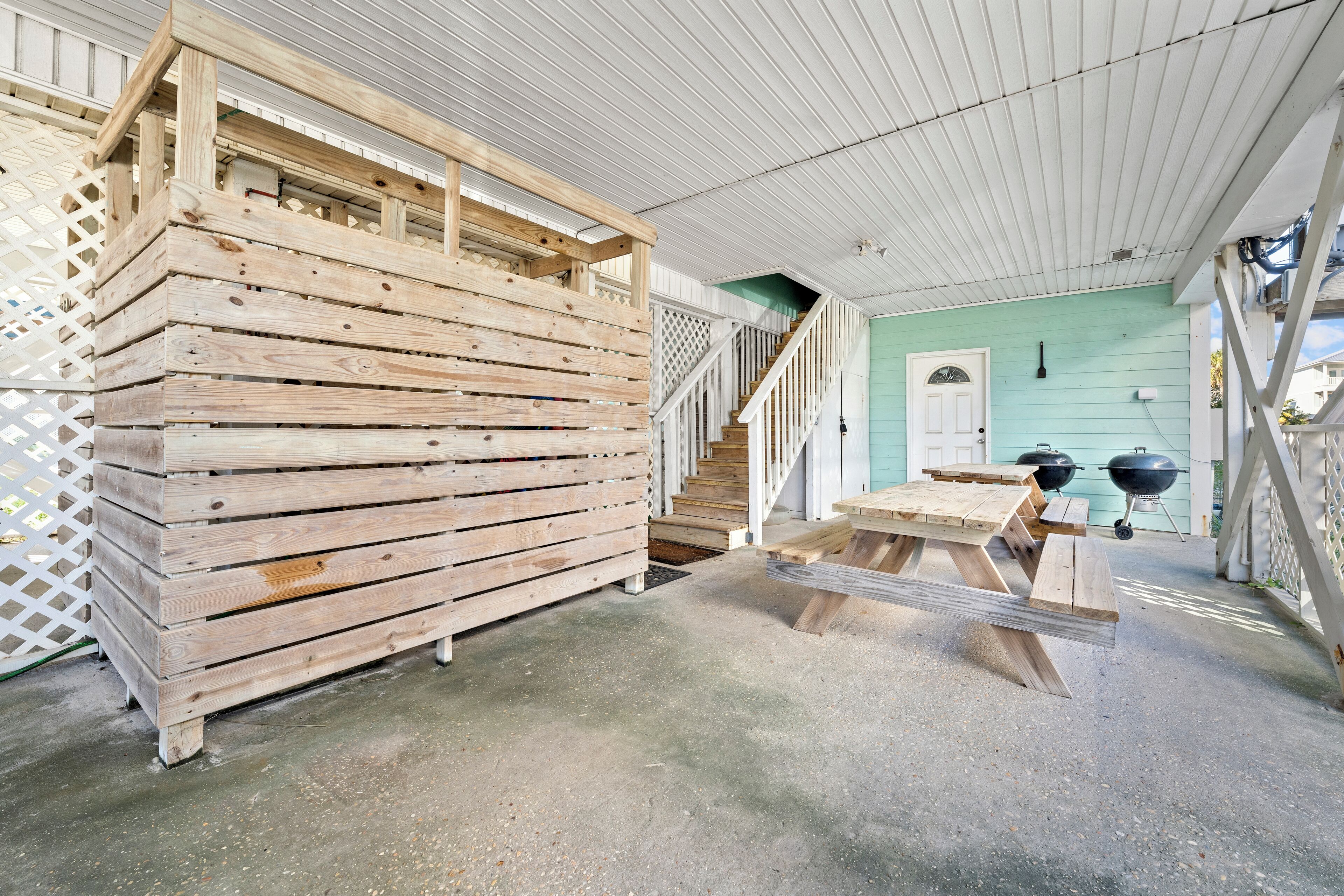 A covered outdoor area with a wooden bench and picnic table, a staircase, and a green building in the background.