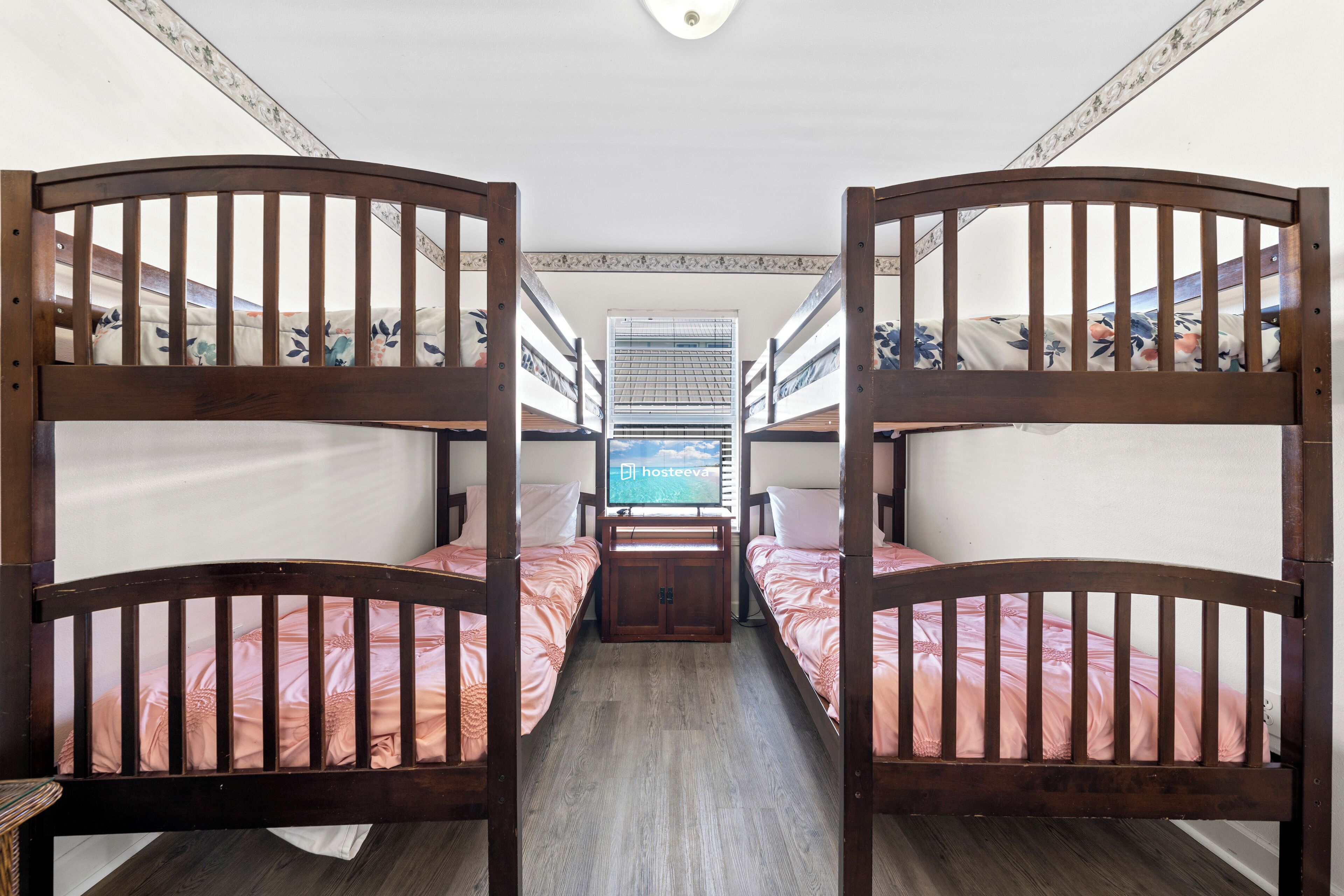 A room with bunk beds, a television, and a window with blinds.