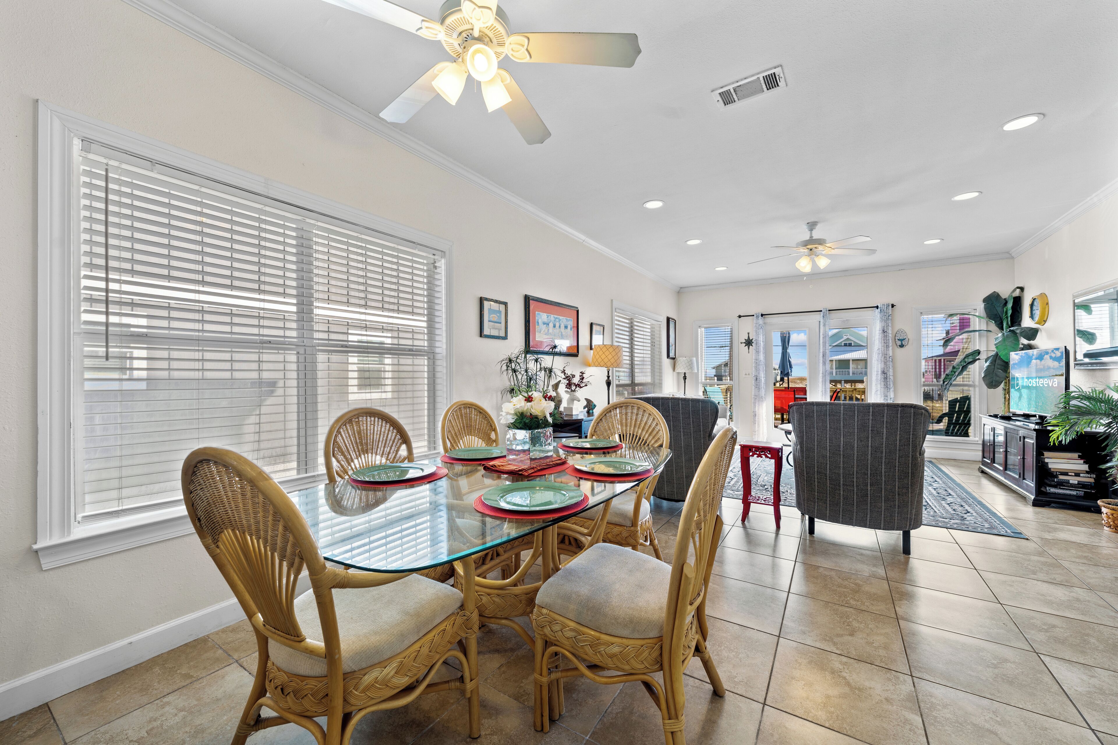 A dining area with a glass table, wicker chairs, and a ceiling fan.