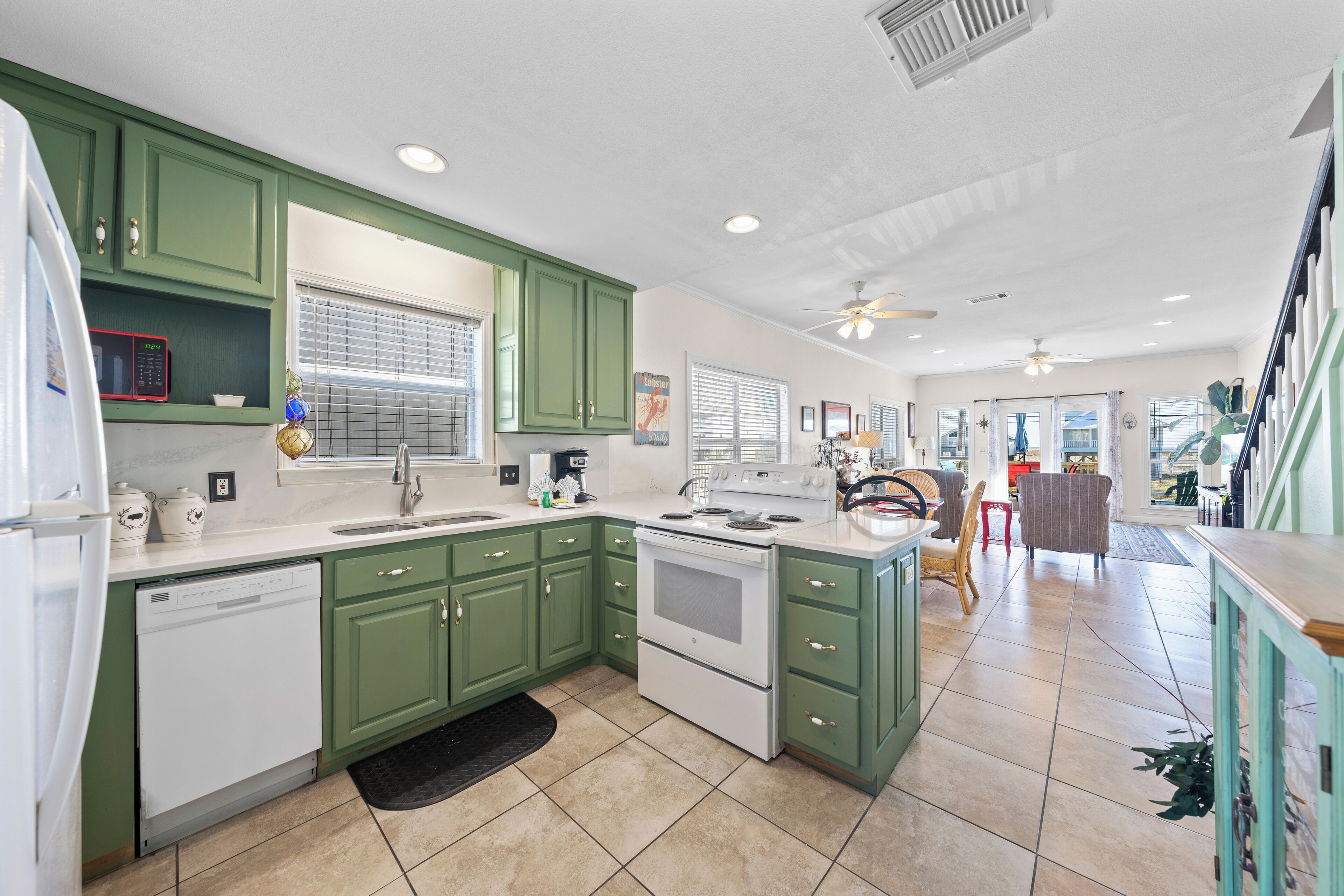 A kitchen with green cabinets, a dishwasher, a stove, and a sink.