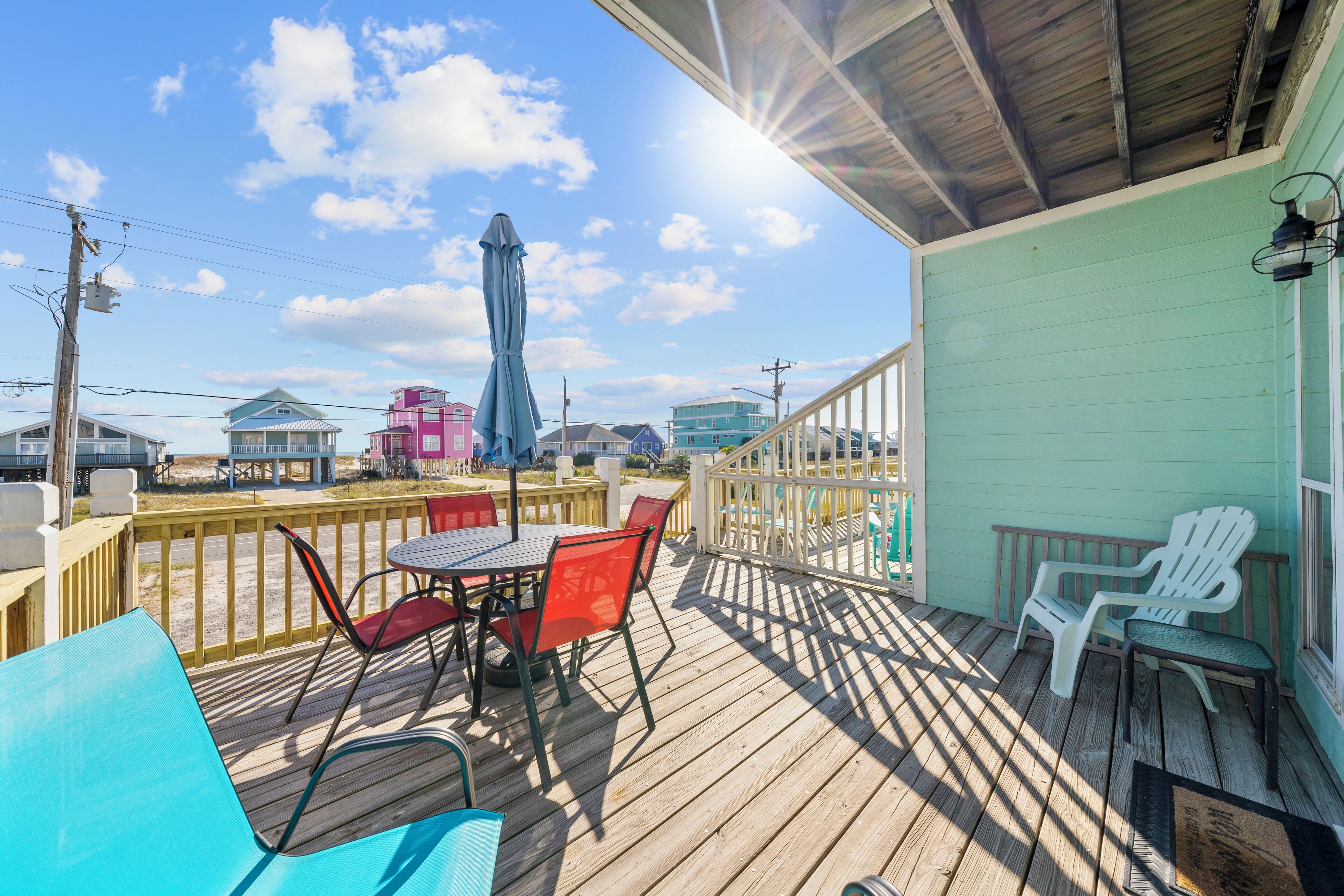 Una terraza de madera con mobiliario exterior, un espacio cubierto y vistas a edificios coloridos al fondo.