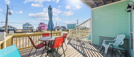 Una terraza de madera con mobiliario exterior, un espacio cubierto y vistas a edificios coloridos al fondo.