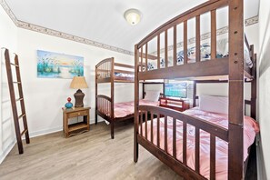Ein Zimmer mit zwei Etagenbetten, einer Holzleiter, einem kleinen Tisch mit Lampe und einem Bild an der Wand.