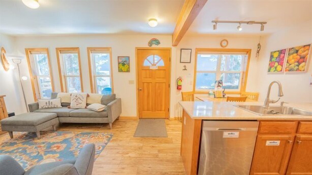 A cozy living room with a sofa, a dining area with a table and chairs, a kitchen with a sink and dishwasher, and large windows. - Townhome in Crested Butte | 3 Bedroom | Walk to Elk Ave | Gas Grill | Parking (Crested Butte)