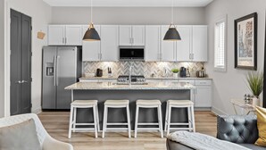 A modern kitchen with white cabinets, a central island with bar stools, a refrigerator, and pendant lighting. - NEW! Sleeps 20+ 2 SideBySide East Nashville Homes! (Nashville)