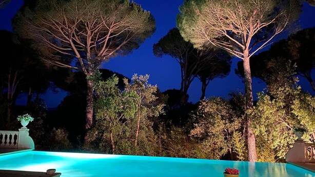 Ein Swimmingpool mit einer klaren blauen Kante, umgeben von Bäumen und einem Nachthimmel.