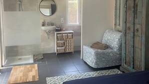 Ein Schlafzimmer mit Bett, Nachttisch, Kleiderschrank, Badezimmer mit Dusche, Waschbecken und Spiegel.