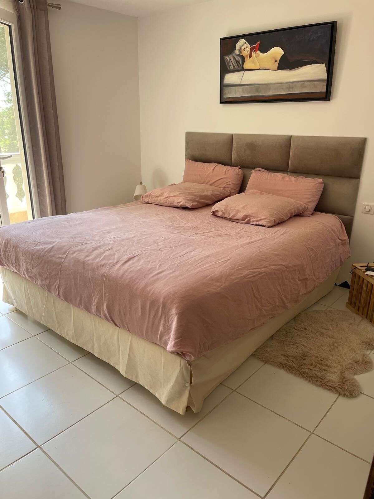 Een slaapkamer met een groot bed, een hoofdbord, een schilderij aan de muur en een raam met gordijnen.
