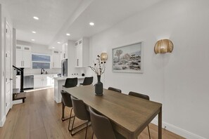 Een moderne keuken met witte kasten, een houten eettafel en een vaas met gedroogde bloemen.