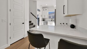 A modern kitchen with white cabinets, a marble countertop, and a black chair. - Eden Townhouse: Hot Tub & Golf Retreat w/Mountain Views (Eden)