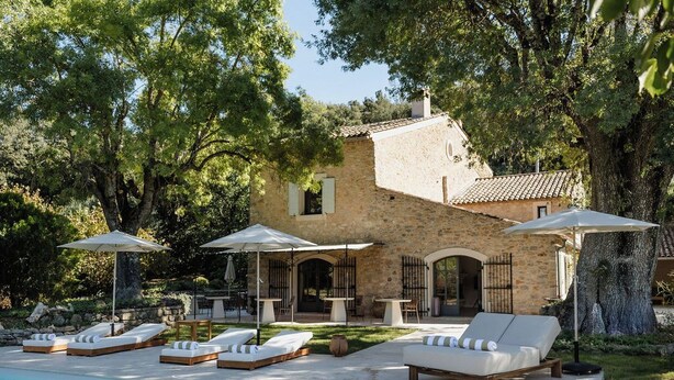 Un edificio in pietra con piscina, lettini e ombrelloni.