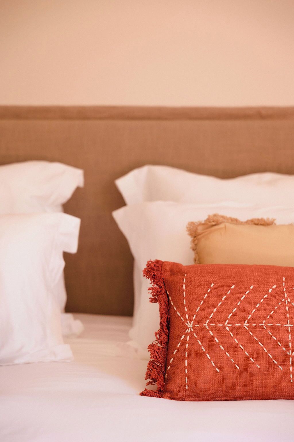 A bed with white bedding and a red pillow with white stitching.