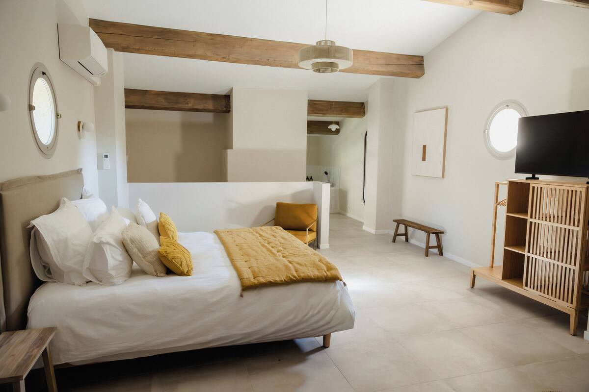A bedroom with a bed, a wooden bench, a TV stand, and a mirror.
