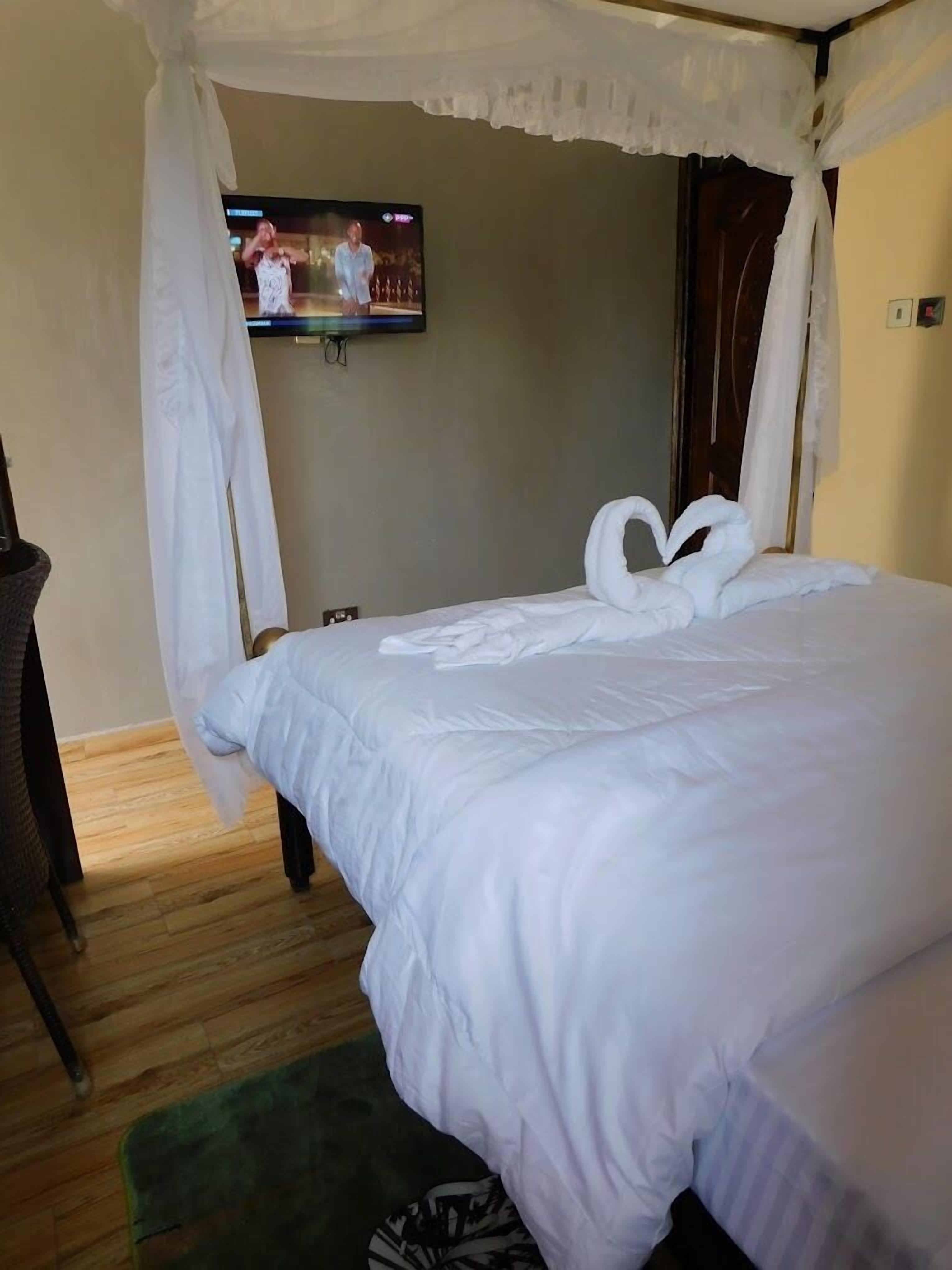 A hotel room with a bed, a television mounted on the wall, and a wooden floor.