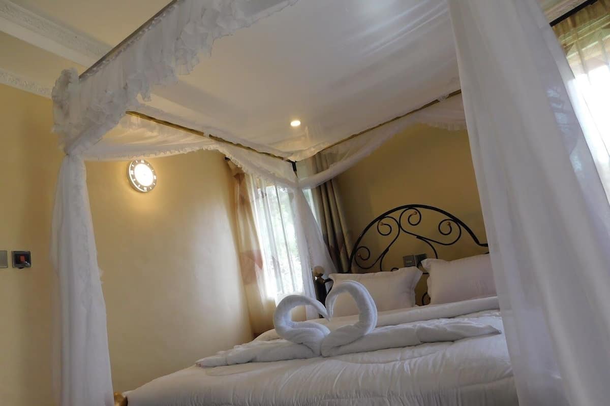 A bed with white bedding and a canopy, a round wall clock, and a bed frame with a decorative headboard.
