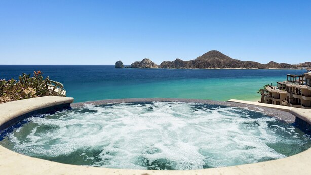 A hot tub with a view of the ocean and a mountainous island in the distance.