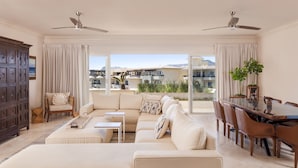 A spacious living room with a large beige sectional sofa, a dining table with chairs, and a ceiling fan.