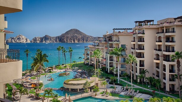 Un complexe hôtelier doté d’une piscine, de palmiers et offrant une vue sur la mer et les montagnes.
