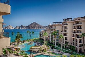 Ein Resort mit Poolanlage, Palmen und Blick auf Meer und Berge.