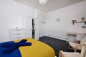 A hotel room with a bed, a desk, a chair, a wardrobe, and a clock on the wall.