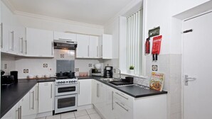 A modern kitchen with white cabinets, a black countertop, a stove, and a sink. There are fire extinguishers and a cookbook on the counter. - Comfortable Room in Shared House (Liverpool)
