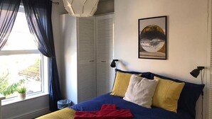 Un dormitorio con una cama, una ventana con cortinas, un armario y un cuadro en la pared.