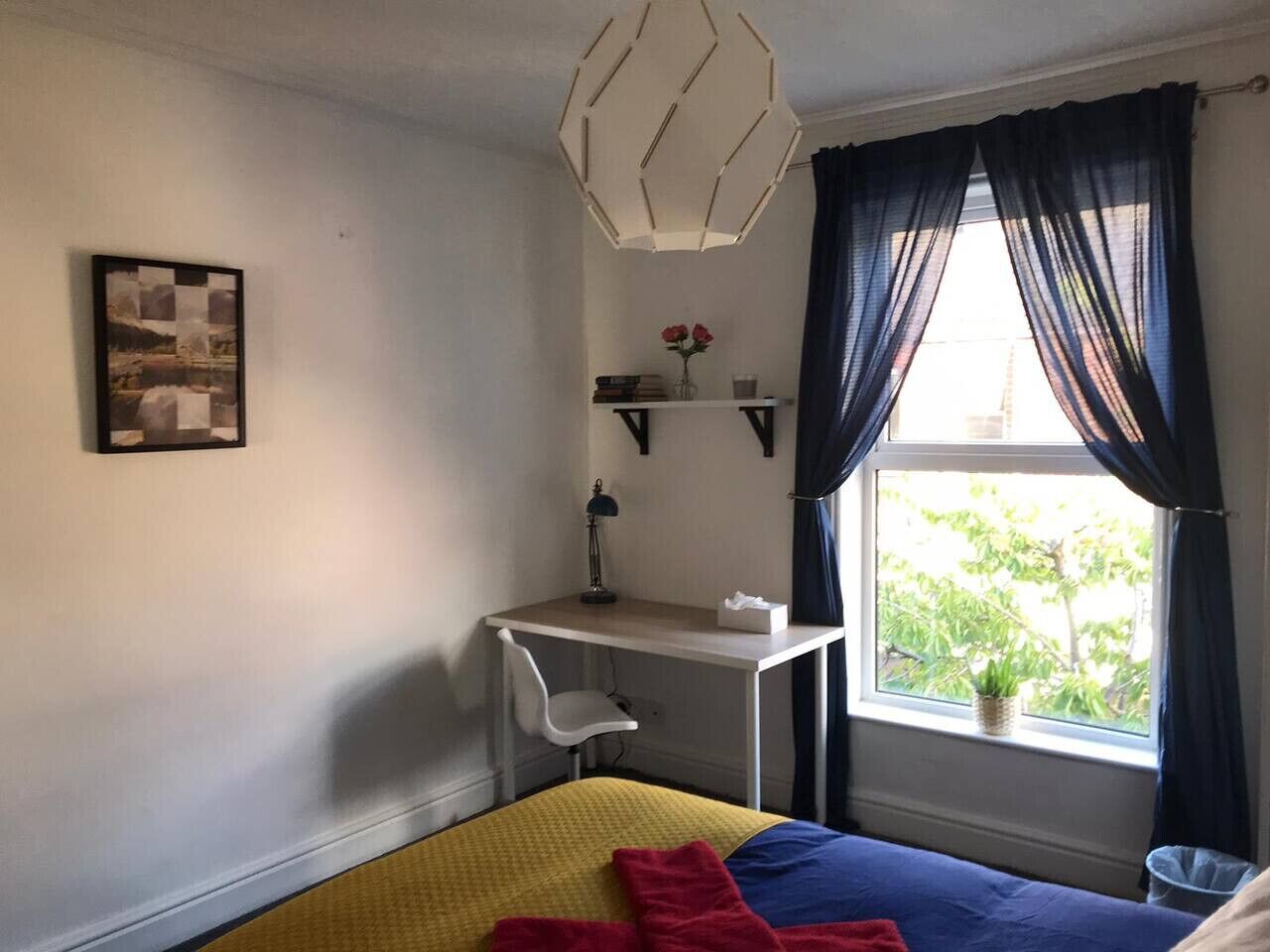 A bedroom with a bed, a desk, and a window with curtains.