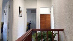 Un pasillo con baranda de madera, una puerta que da a un dormitorio y una planta al frente.