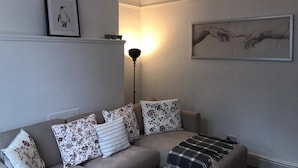 Una sala de estar con sofá, almohadones, lámpara de pie y cuadros en la pared.