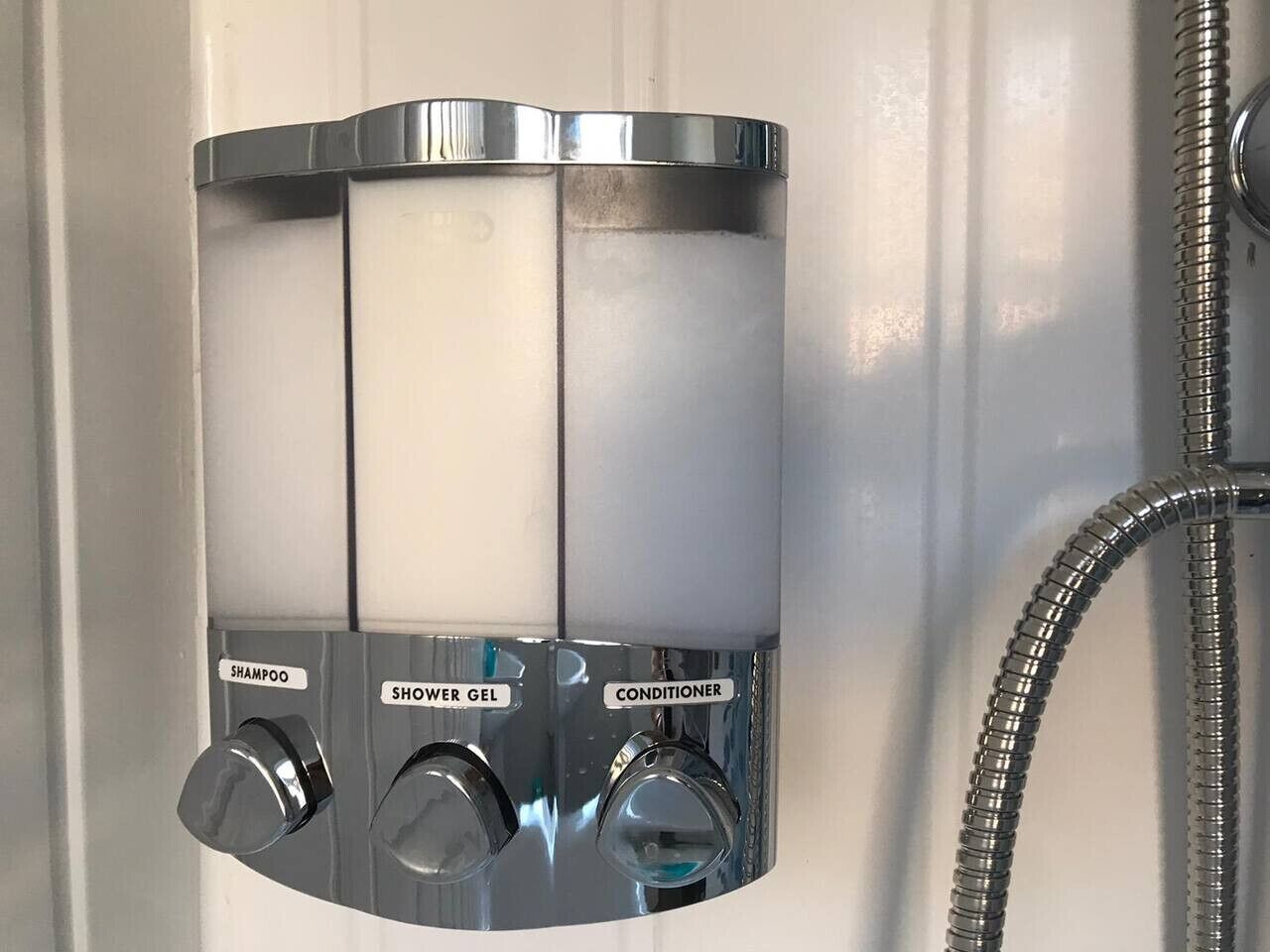 A shower with three knobs labeled for shampoo, shower gel, and conditioner.
