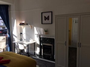 A room with a bed, a desk, a fireplace, and a door leading to another room.