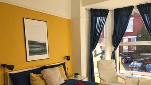 Une chambre d’hôtel avec un lit, une chaise, une table et une fenêtre avec des rideaux.