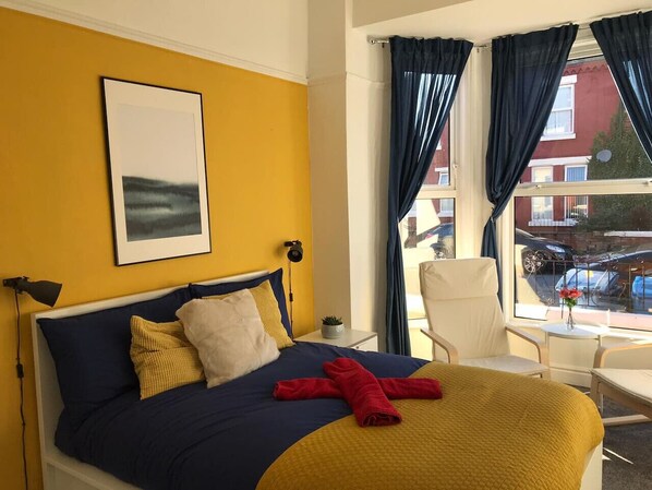 A hotel room with a bed, a chair, a table, and a window with curtains.