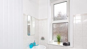 Een badkamer met een witte wastafel, toilet en badkuip. Er is een raam met gezandstraald glas en een plant op de vensterbank.