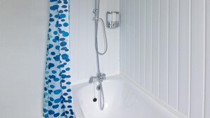 Een badkamer met een douche, een bad en een gordijn met een blauw stippenpatroon.