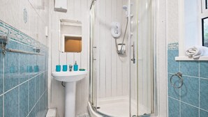 Een badkamer met een douche met glazen wand, een wastafel met toiletartikelen en een handdoekrek.