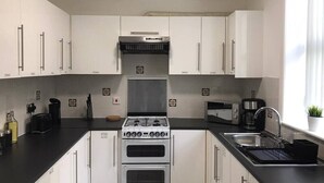 A modern kitchen with white cabinets, a gas stove, a built-in oven, a coffee maker, and a sink. - Experience Comfort in Liverpool (Merseyside)
