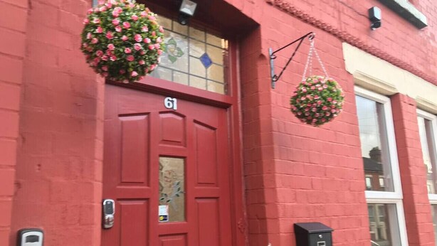 A red door with the number 61, a mailbox, and hanging flower baskets. - Experience Comfort in Liverpool (Merseyside)