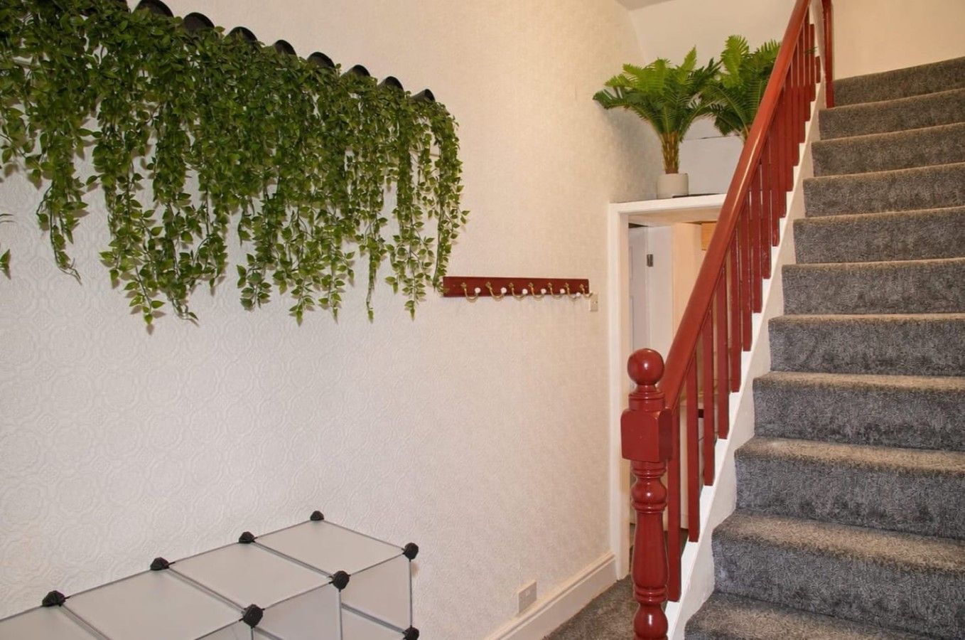 Una escalera con barandilla roja y peldaños alfombrados, una planta colgante en la pared y una decoración geométrica.