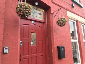 A red door with the number 61, a hanging flower basket, and a black intercom box. - Close to City Centre Shared Bath (Merseyside)