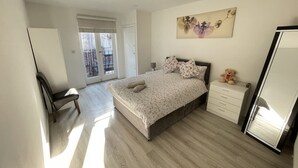 Een slaapkamer met een bed, een dressoir, een stoel en een groot raam met jaloezieën.