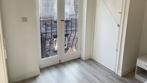 Een kamer met een schuifglasdeur naar een balkon, een witte deur en een licht houten vloer.