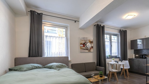 A compact bedroom with a bed, a small sofa, a dining table with chairs, and a kitchenette.