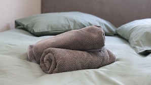 A bed with a green pillow and a folded brown towel.