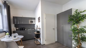 A compact kitchen with a microwave, a sink, and a coffee machine. There is a dining table with chairs and a potted plant.