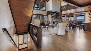 Un vaste espace de vie doté d’une cheminée, de parquets en bois et de grandes fenêtres offrant une vue sur l’extérieur.