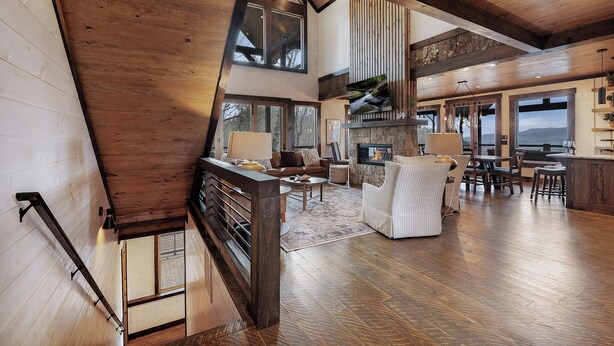 A spacious living area with a fireplace, wooden flooring, and large windows offering views of the outdoors.