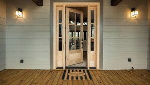 Une porte en bois avec des panneaux de verre donnant sur une pièce, un paillasson et deux lampes fixées au mur.