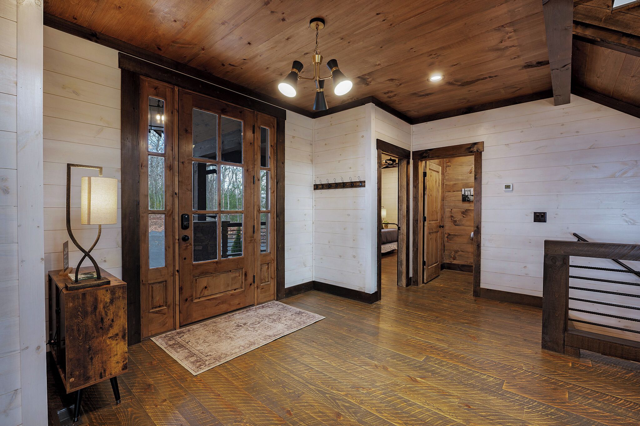 Ein Holzinterieur mit einer großen Tür, einem kleinen Tisch mit Lampe und einer Bank.